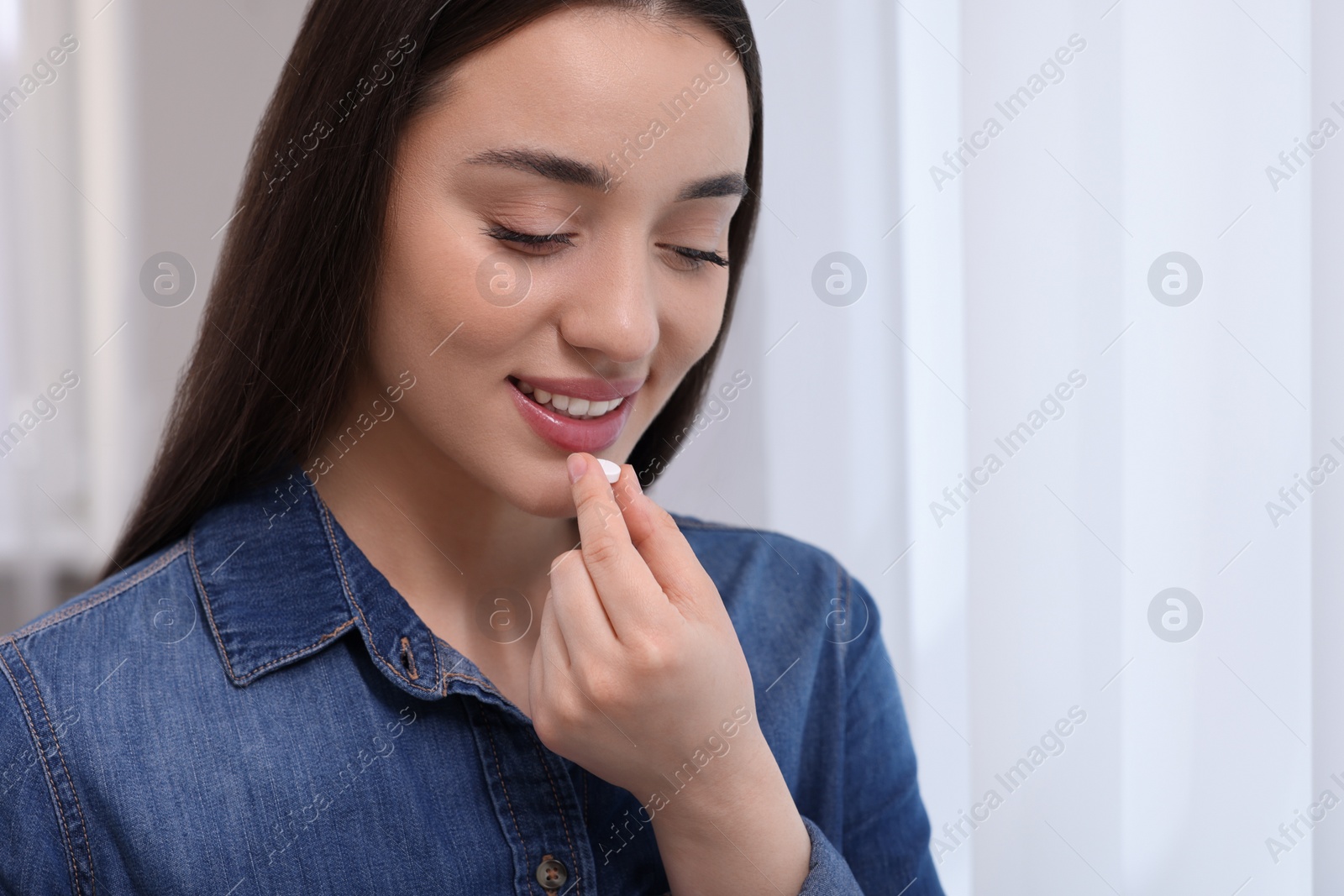 Photo of Beautiful young woman taking pill indoors, space for text