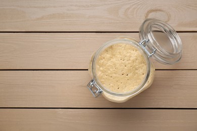 Photo of Leaven in glass jar on beige wooden table, top view. Space for text