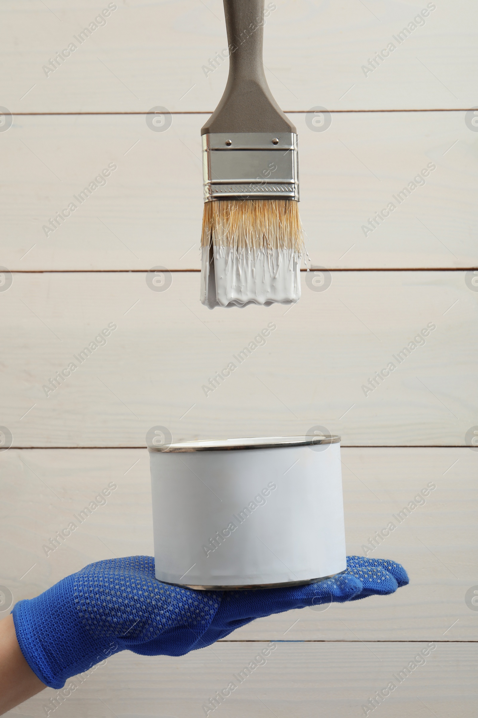 Photo of Worker with can of white paint and brush against wooden background, closeup