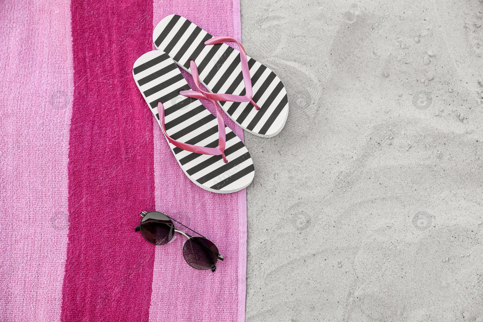 Photo of Towel with stylish flip flops and sunglasses on sand, flat lay. Space for text