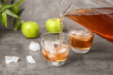 Photo of Apple juice pouring from jug into glass with ice cubes on table