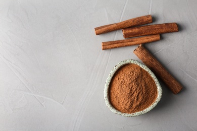 Photo of Bowl with aromatic cinnamon powder and sticks on grey background