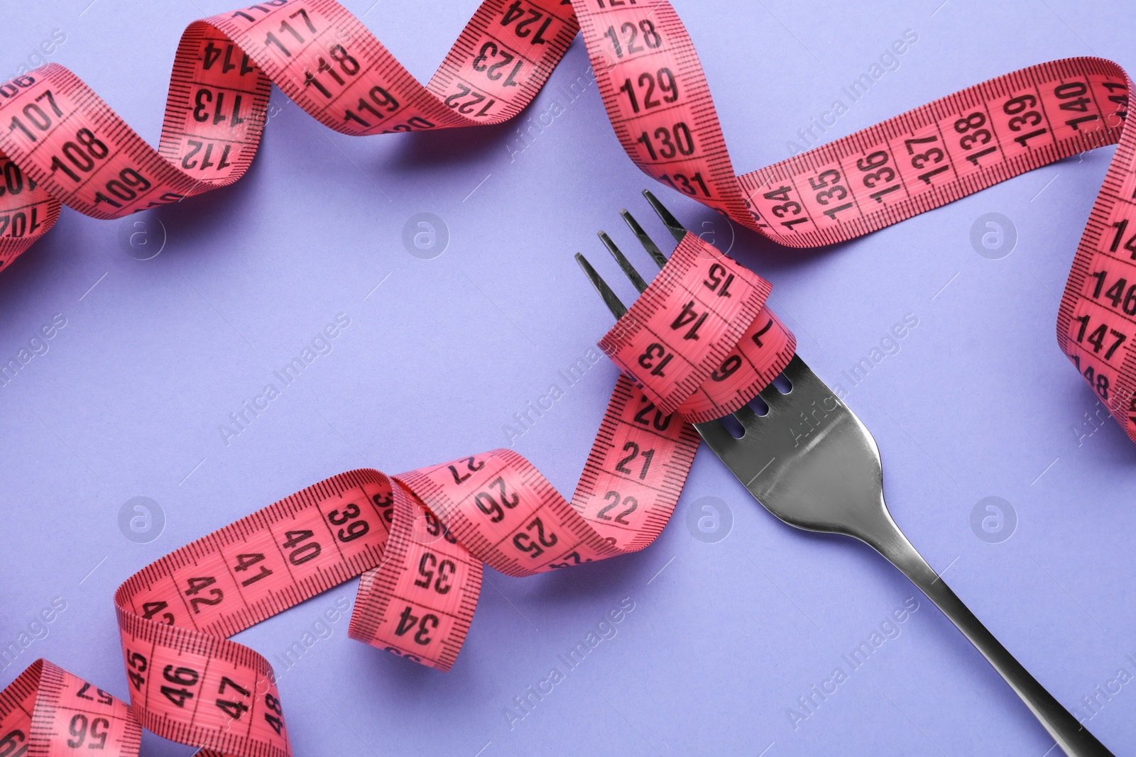 Photo of Fork with measuring tape on violet background, top view. Diet concept