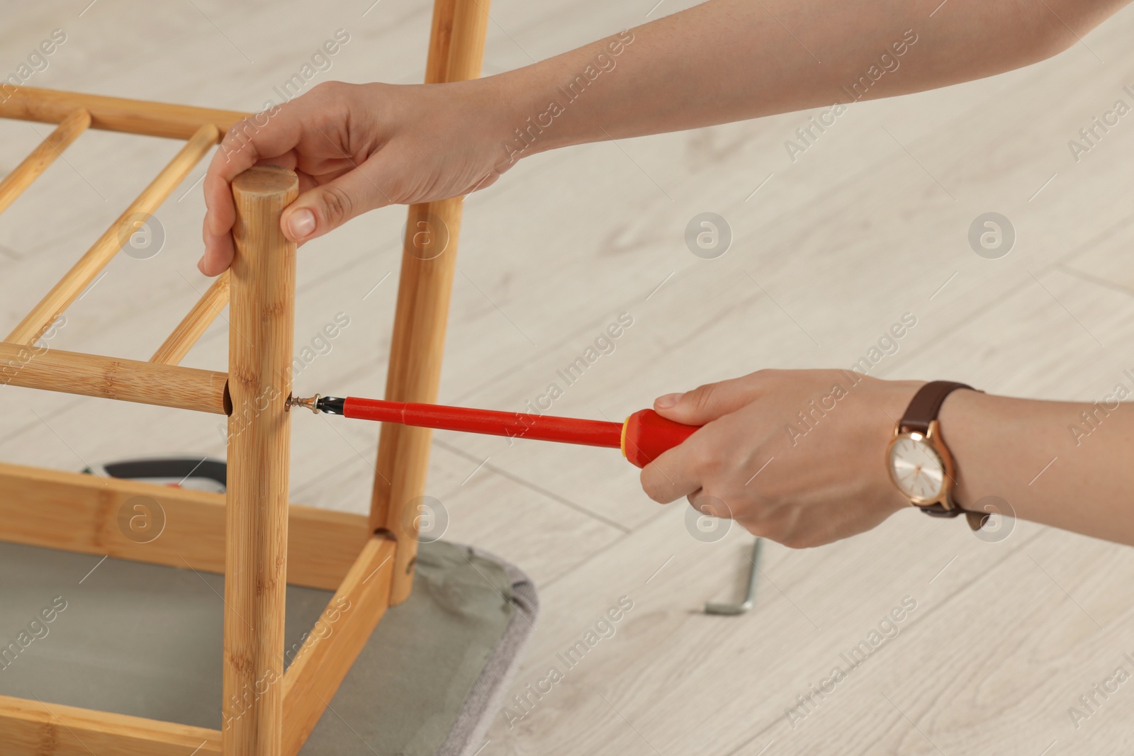 Photo of Woman with screwdriver assembling furniture on floor, closeup