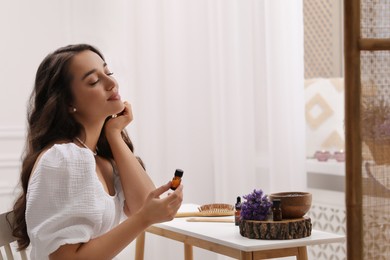 Beautiful young woman with bottle of essential oil at table in room