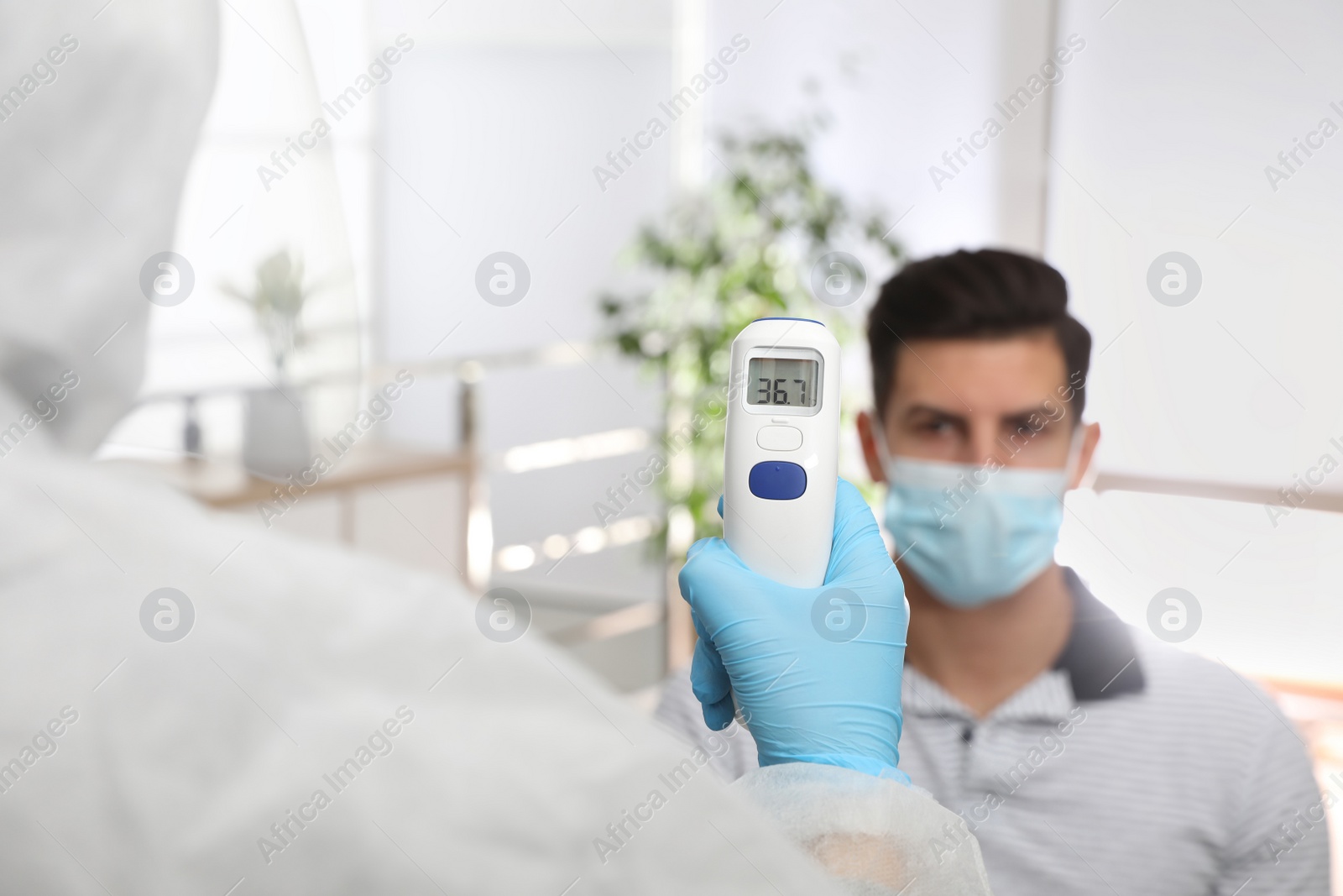 Photo of Doctor measuring man's temperature in office, closeup. Prevent spreading of Covid-19