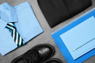 Stylish school uniform for boy and stationery on grey background, flat lay