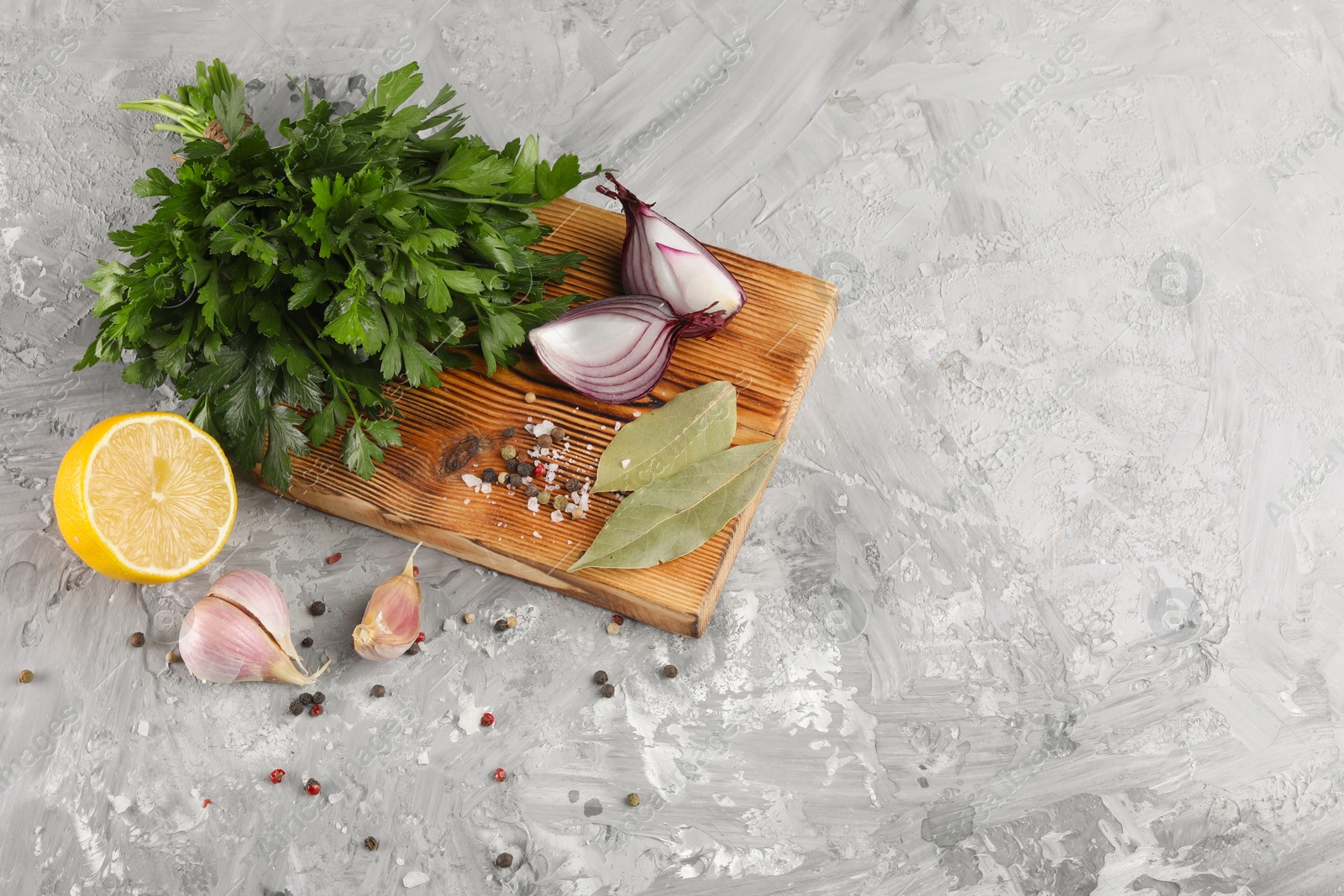 Photo of Bunch of fresh parsley, lemon, onion, garlic and spices on grey textured table, above view. Space for text