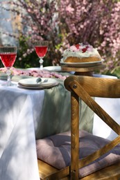 Beautiful spring flowers, delicious cake and wine glasses on table in garden