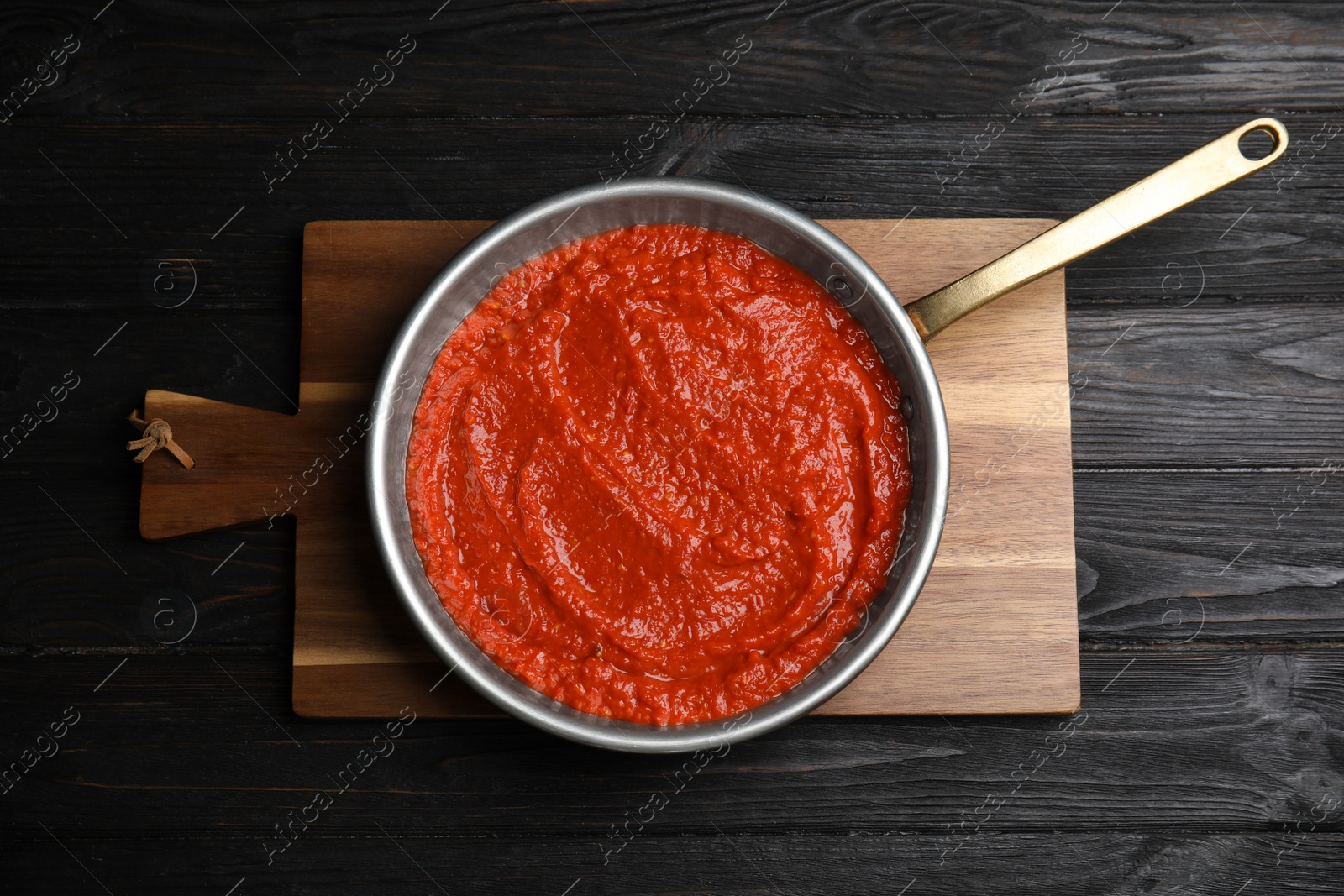 Photo of Delicious tomato sauce in pan on black wooden table, top view