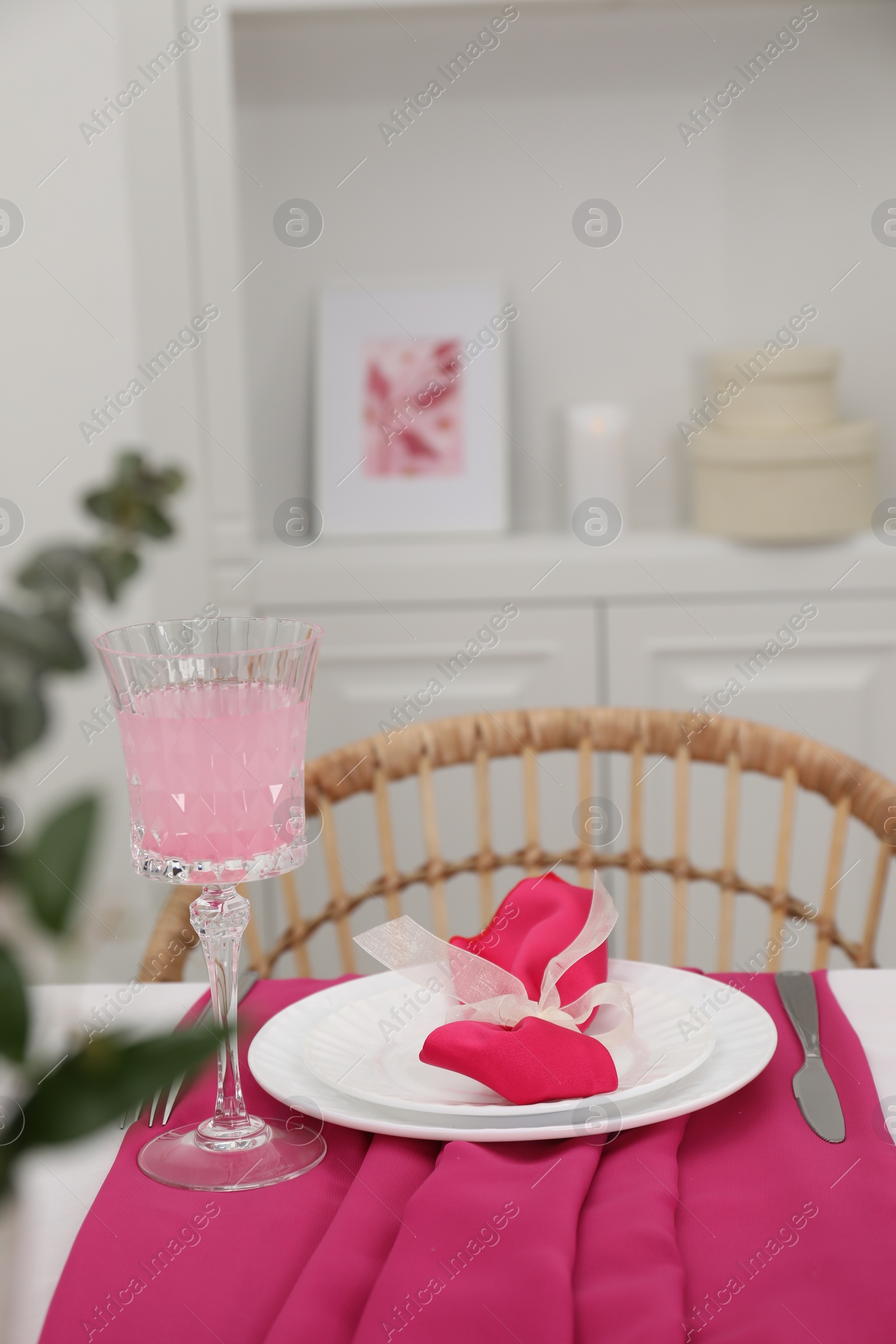 Photo of Table setting. Glass of tasty beverage, plates with pink napkin and cutlery in dining room