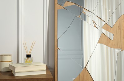 Photo of Broken mirror, reed diffuser and books on wooden table in room