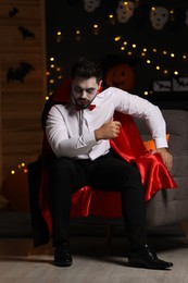 Photo of Man in scary vampire costume against blurred lights indoors. Halloween celebration