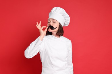 Photo of Confectioner with funny artificial moustache showing ok gesture on red background