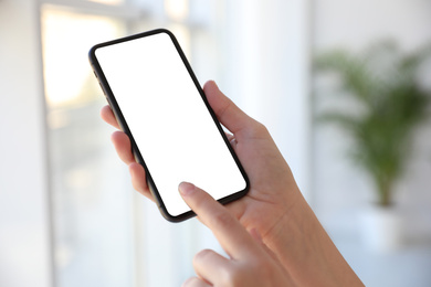 Woman holding mobile phone with empty screen indoors, closeup