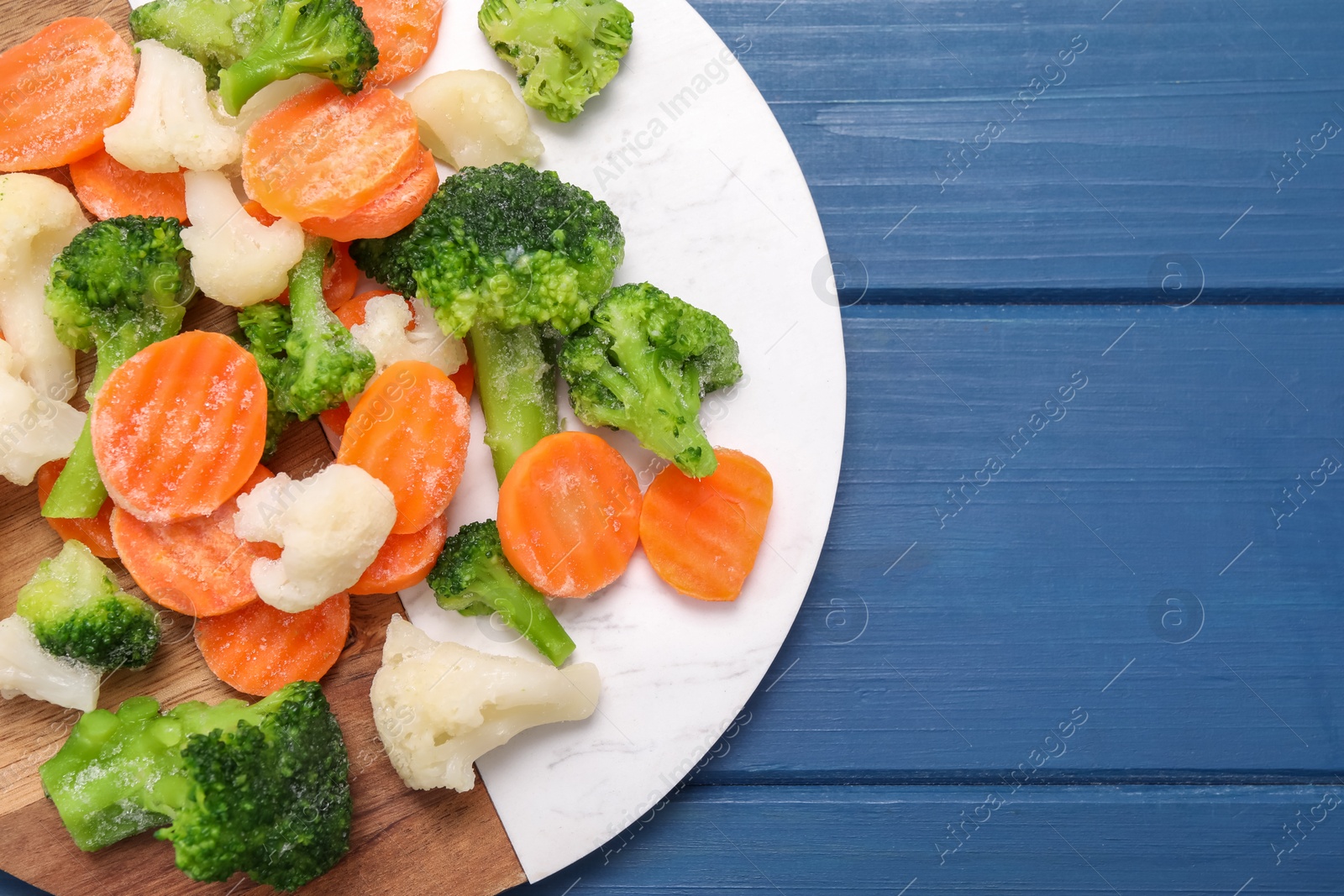 Photo of Mix of different frozen vegetables on blue wooden table, top view. Space for text