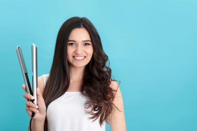 Photo of Young woman with modern hair iron on blue background, space for text