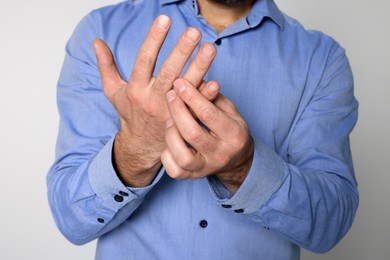 Photo of Man suffering from pain in his hand on light background, closeup. Arthritis symptoms