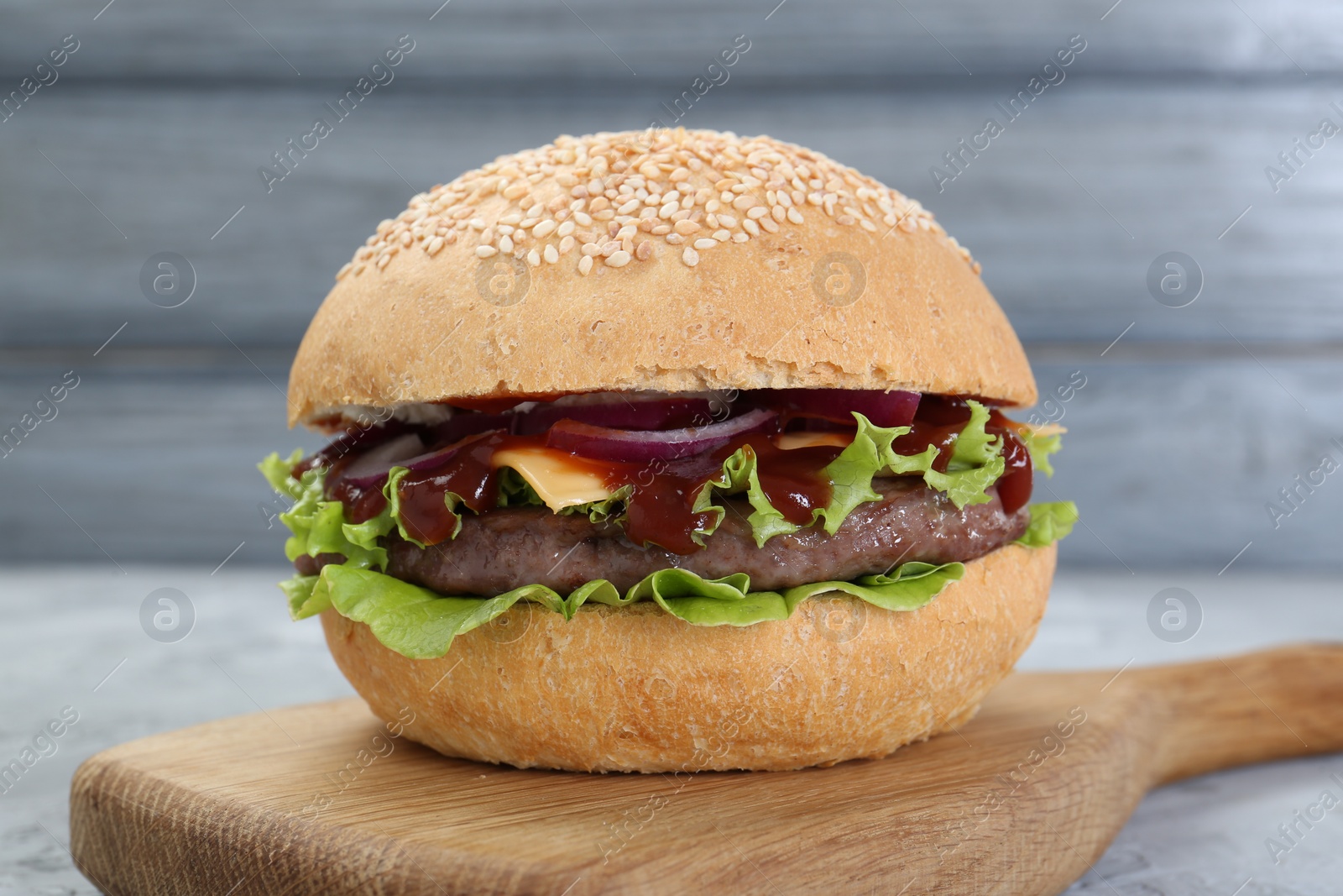 Photo of Delicious cheeseburger with lettuce, onion, ketchup and patty on table, closeup