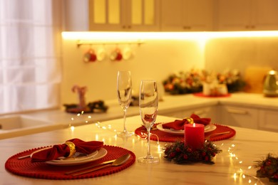 Photo of Christmas table setting with burning candles and festive decor in kitchen