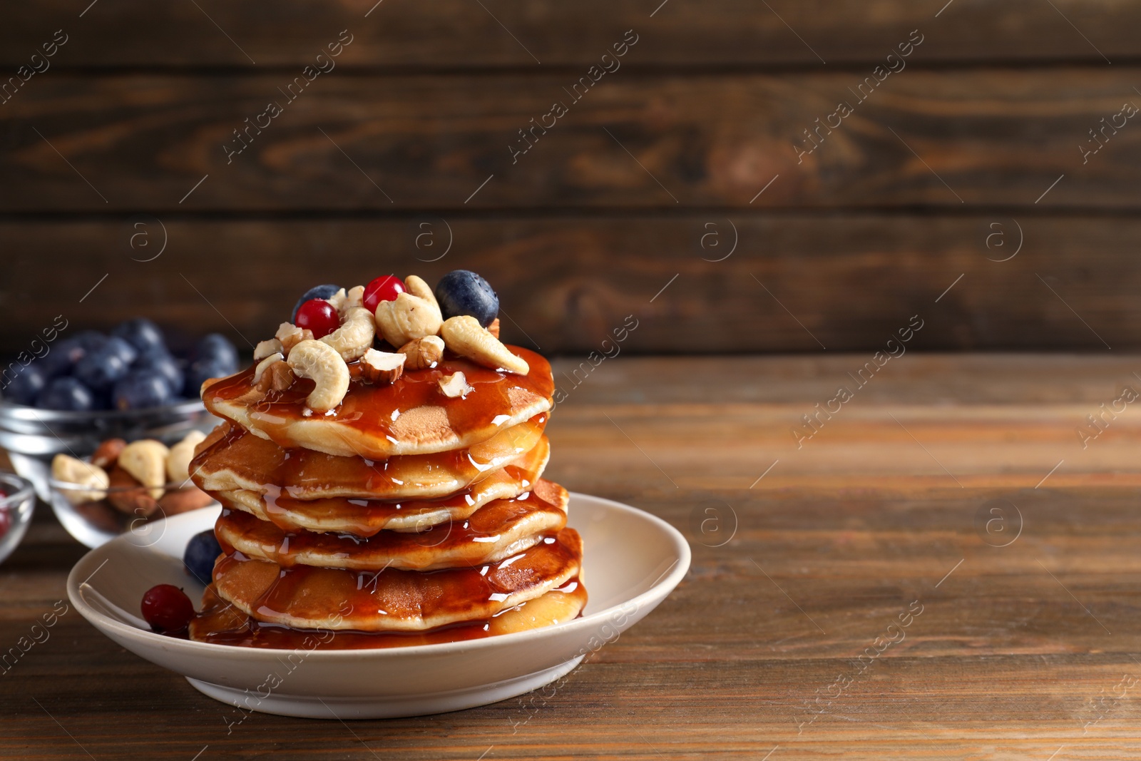 Photo of Stack of tasty pancakes with berries, nuts and syrup on table