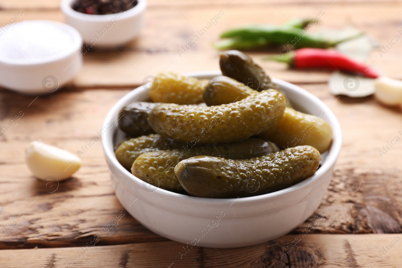 Photo of Bowl of pickled cucumbers and ingredients for food preservation on wooden table, closeup