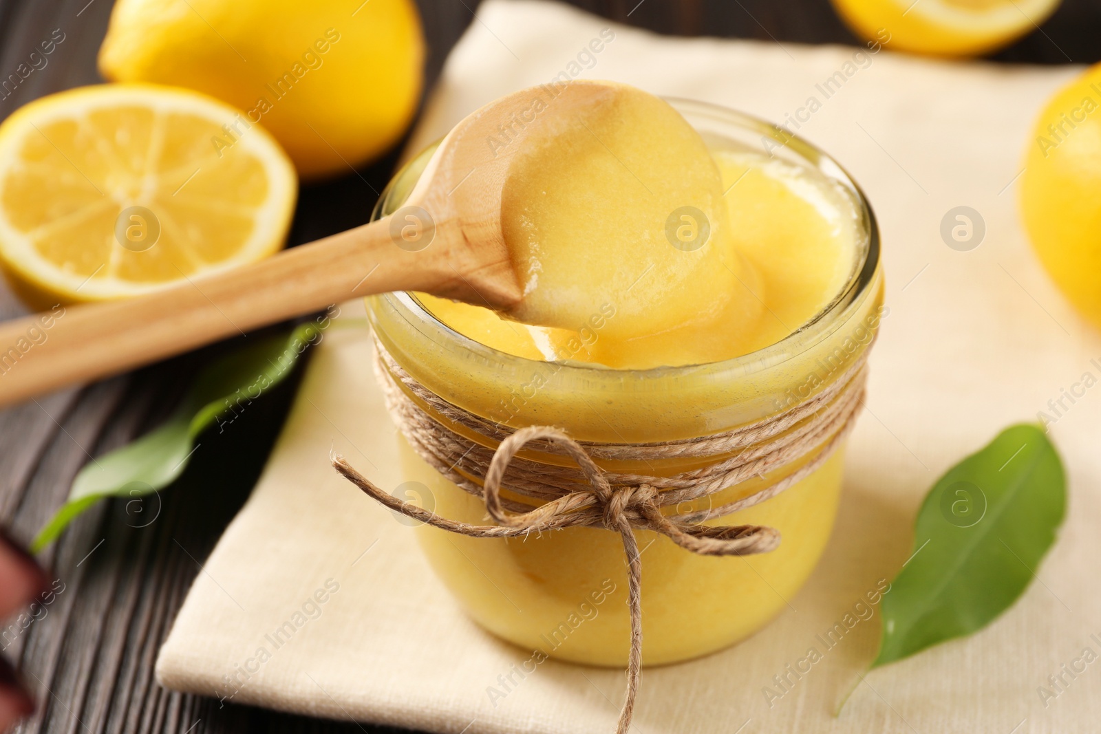 Photo of Taking delicious lemon curd from glass jar at wooden table, closeup