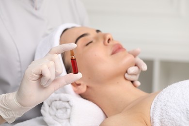 Professional cosmetologist holding skincare ampoule while working with client in clinic, closeup