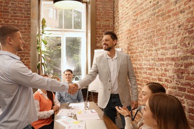 Photo of Office employees shaking hands during meeting at work