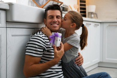 Photo of Man receiving gift for Father's Day from his daughter in kitchen