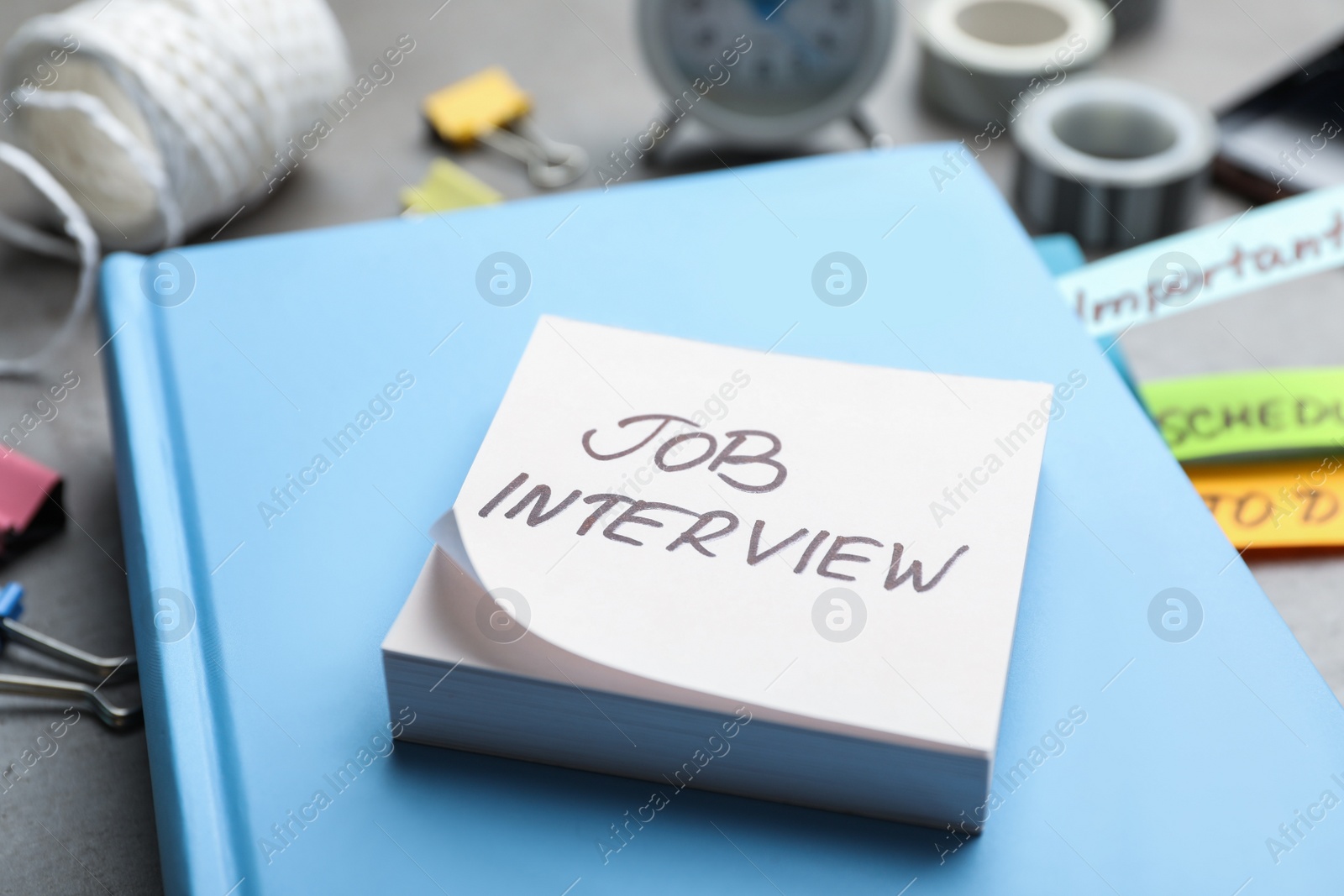 Photo of Reminder note about job interview and stationery on table, closeup