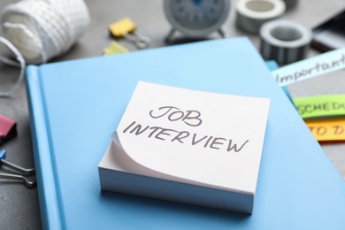 Photo of Reminder note about job interview and stationery on table, closeup