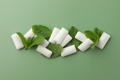 Photo of Tasty white chewing gums and mint leaves on light green background, flat lay