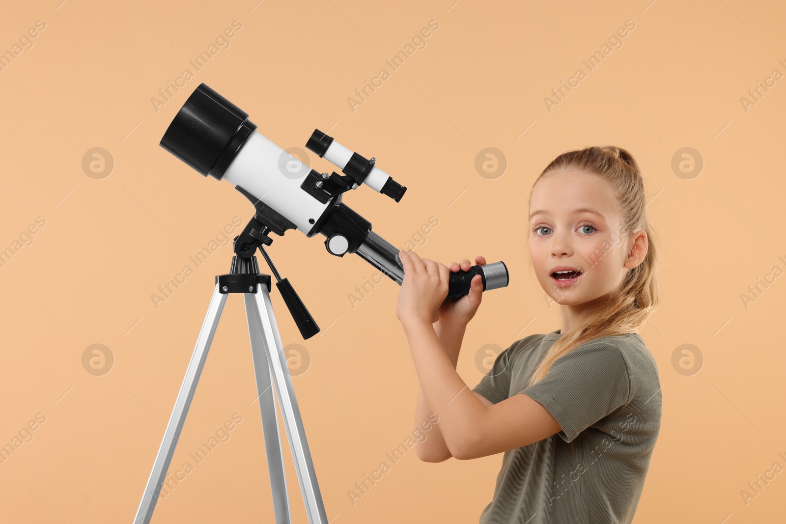 Photo of Surprised little girl with telescope on beige background