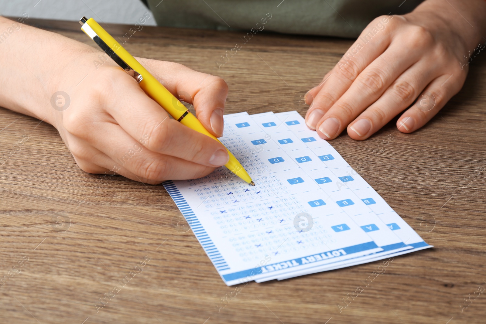 Photo of Woman filling out lottery tickets with pen on wooden table, closeup