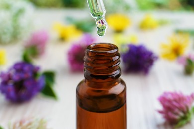 Dripping essential oil from pipette into bottle on white wooden table, closeup