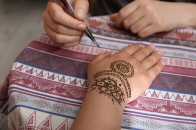 Photo of Master making henna tattoo on hand, closeup. Traditional mehndi