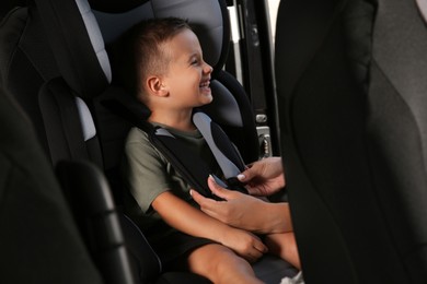 Mother fastening her son with car safety belt in child seat, closeup