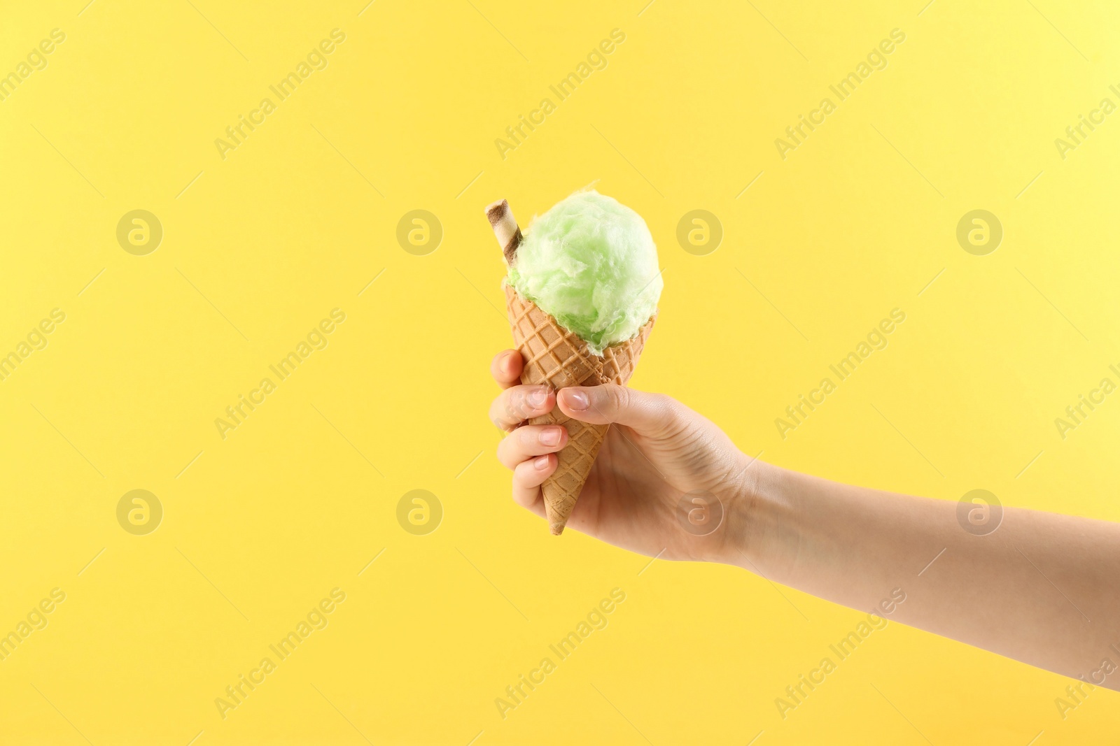 Photo of Woman holding waffle cone with cotton candy on yellow background, closeup