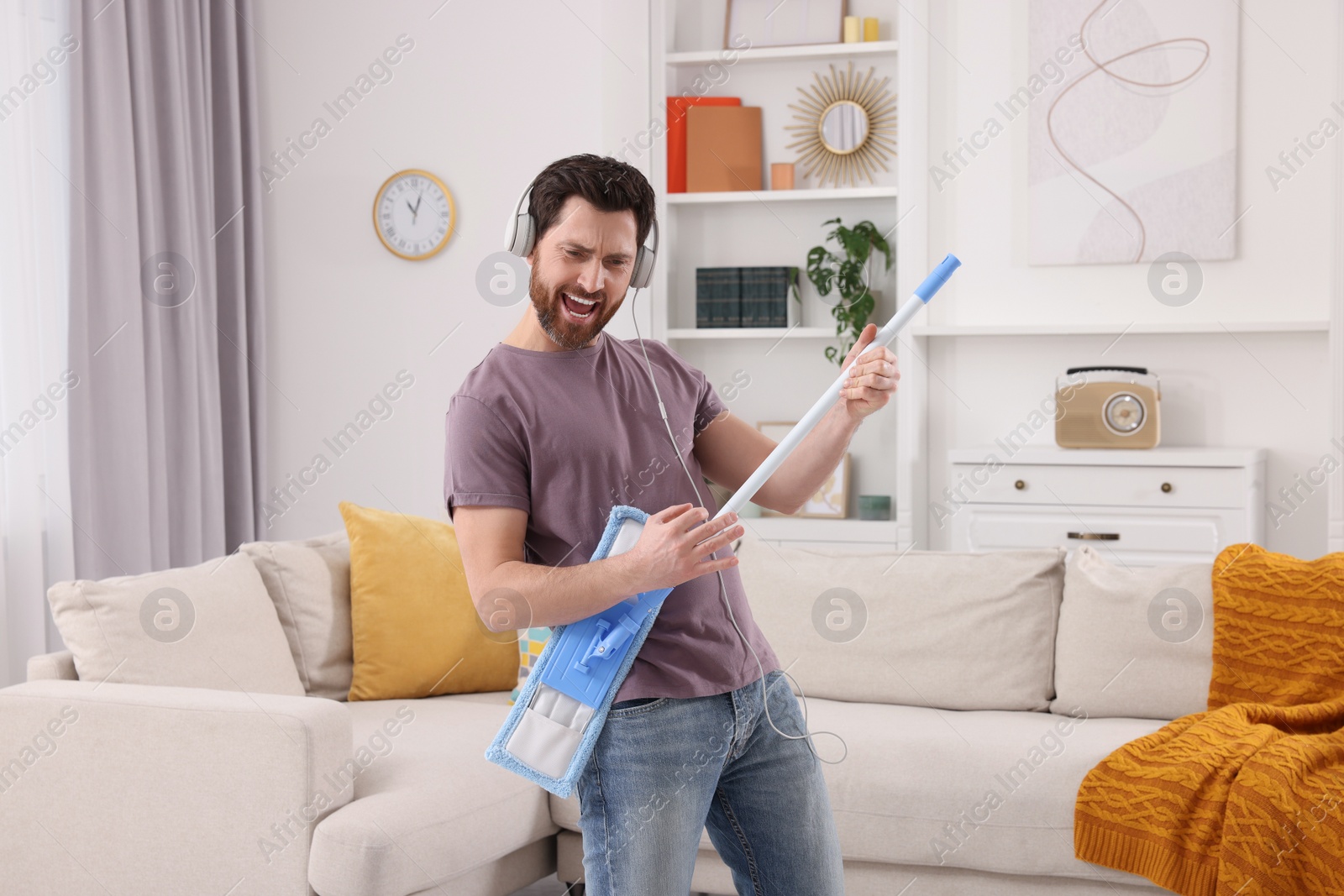 Photo of Spring cleaning. Man in headphones with mop singing while tidying up living room