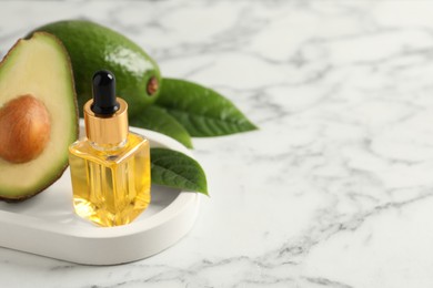 Photo of Bottle of essential oil and avocados on white marble table. Space for text