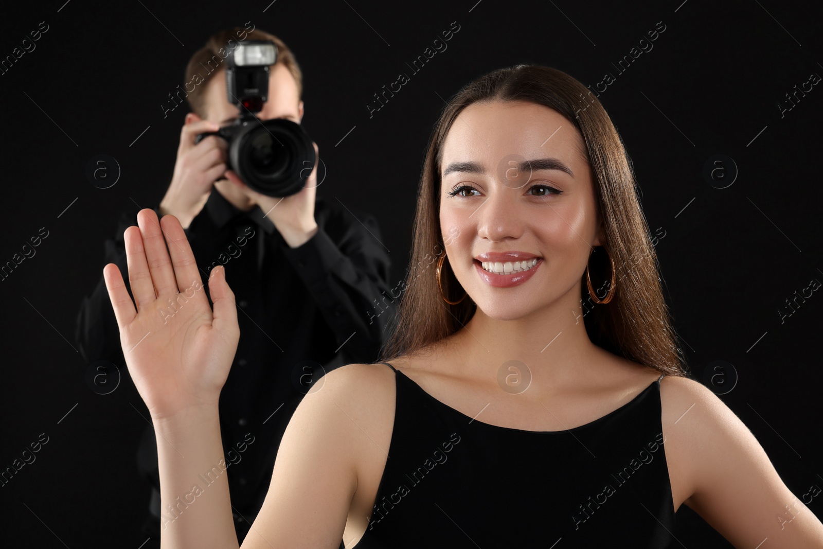 Photo of Professional photographer taking picture of beautiful young woman on black background, selective focus