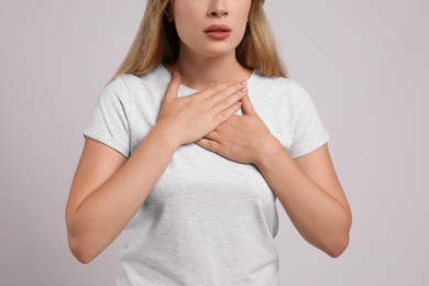 Photo of Young woman suffering from pain during breathing on light grey background, closeup