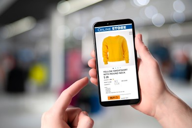 Man visiting shop to take ordered sweatshirt indoors, closeup. Online store website on device screen