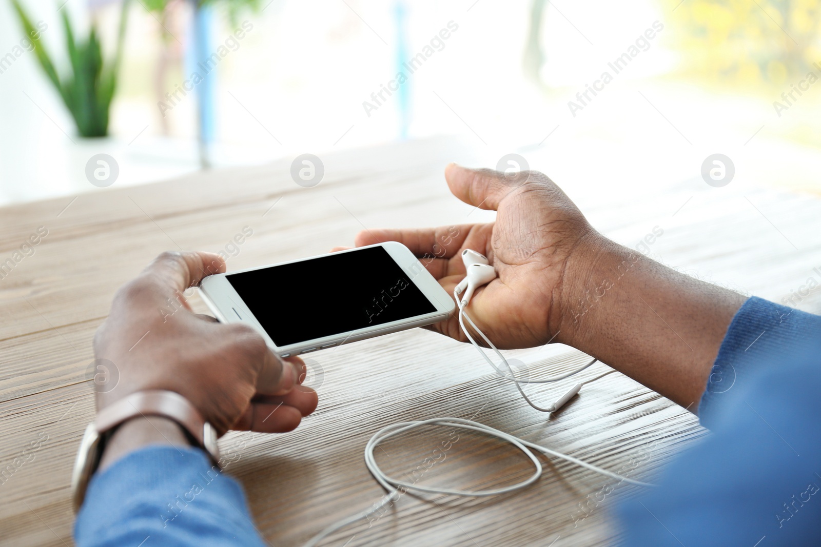 Photo of African-American man holding mobile phone with blank screen in hands at table indoors