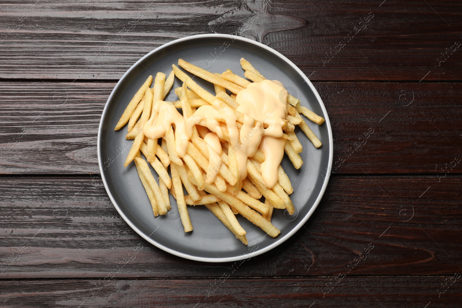 Photo of Delicious french fries with cheese sauce on wooden table, top view