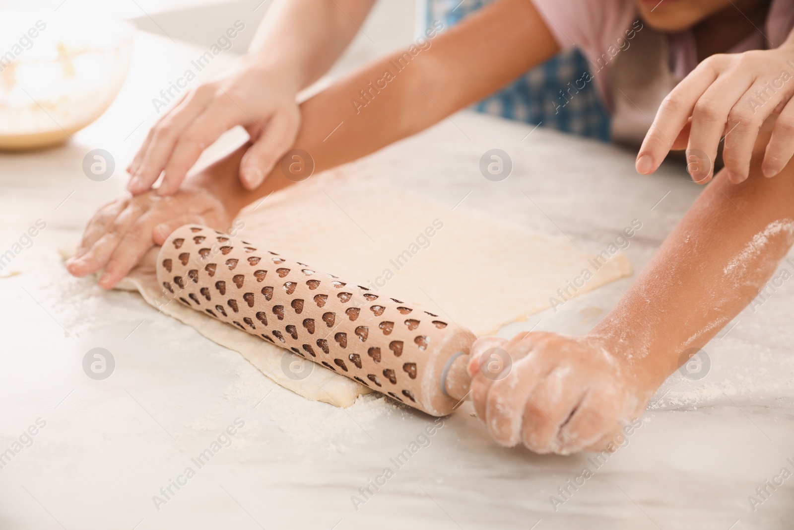 Photo of Mother and daughter rolling dough together at table, closeup