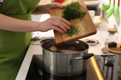 Photo of Woman putting dill into pot to make bouillon in kitchen, closeup. Homemade recipe