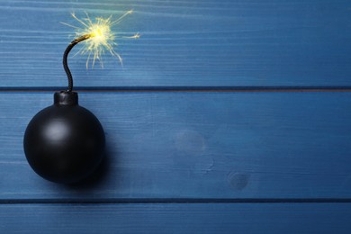 Image of Old fashioned black bomb with lit fuse on blue wooden table, top view. Space for text