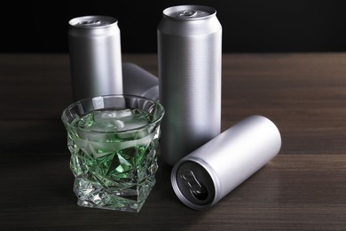 Photo of Energy drink with ice cubes in glass and aluminium cans on wooden table